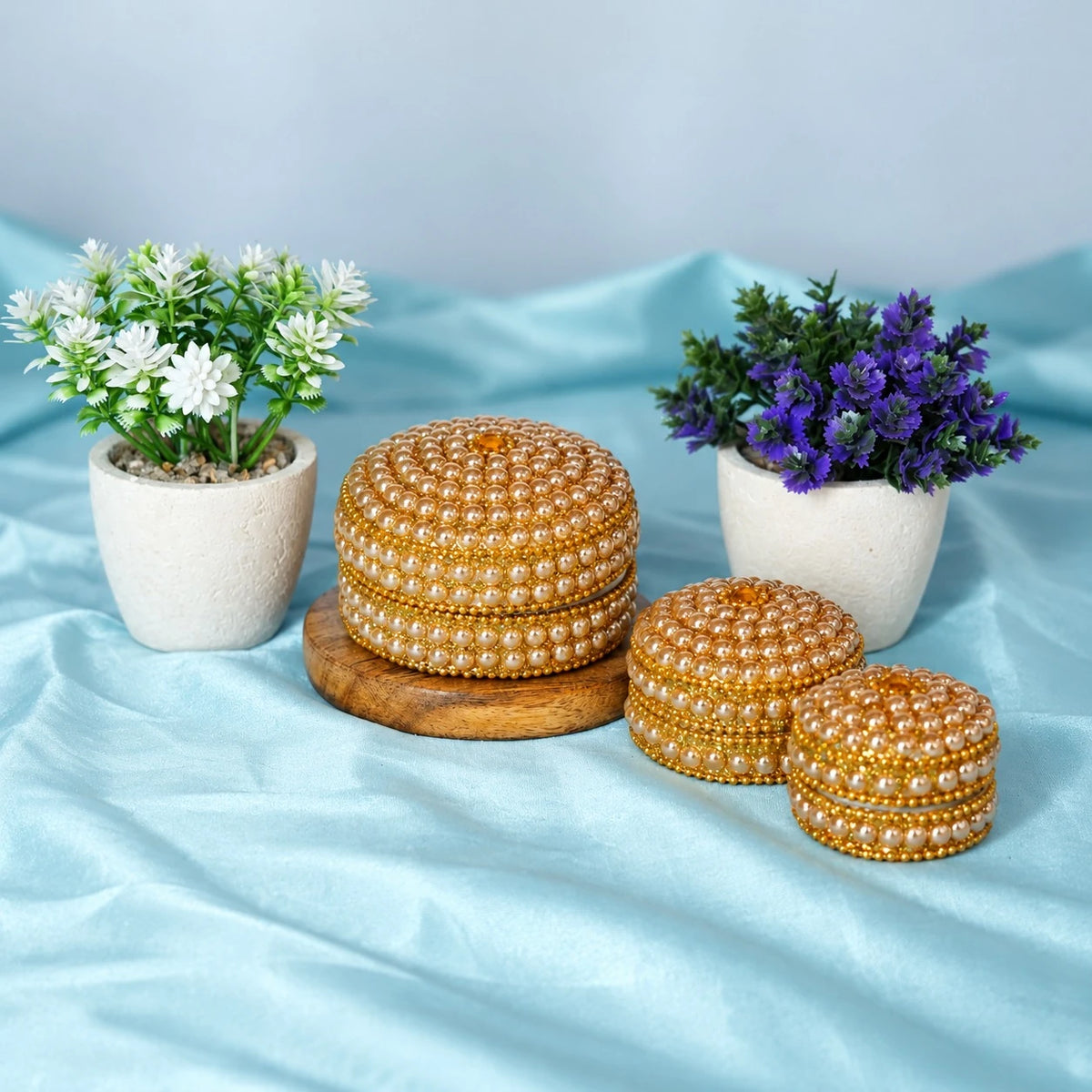 Set of three round beaded pujan dibbi boxes in large, medium and small sizes, with the large one on a wooden base
