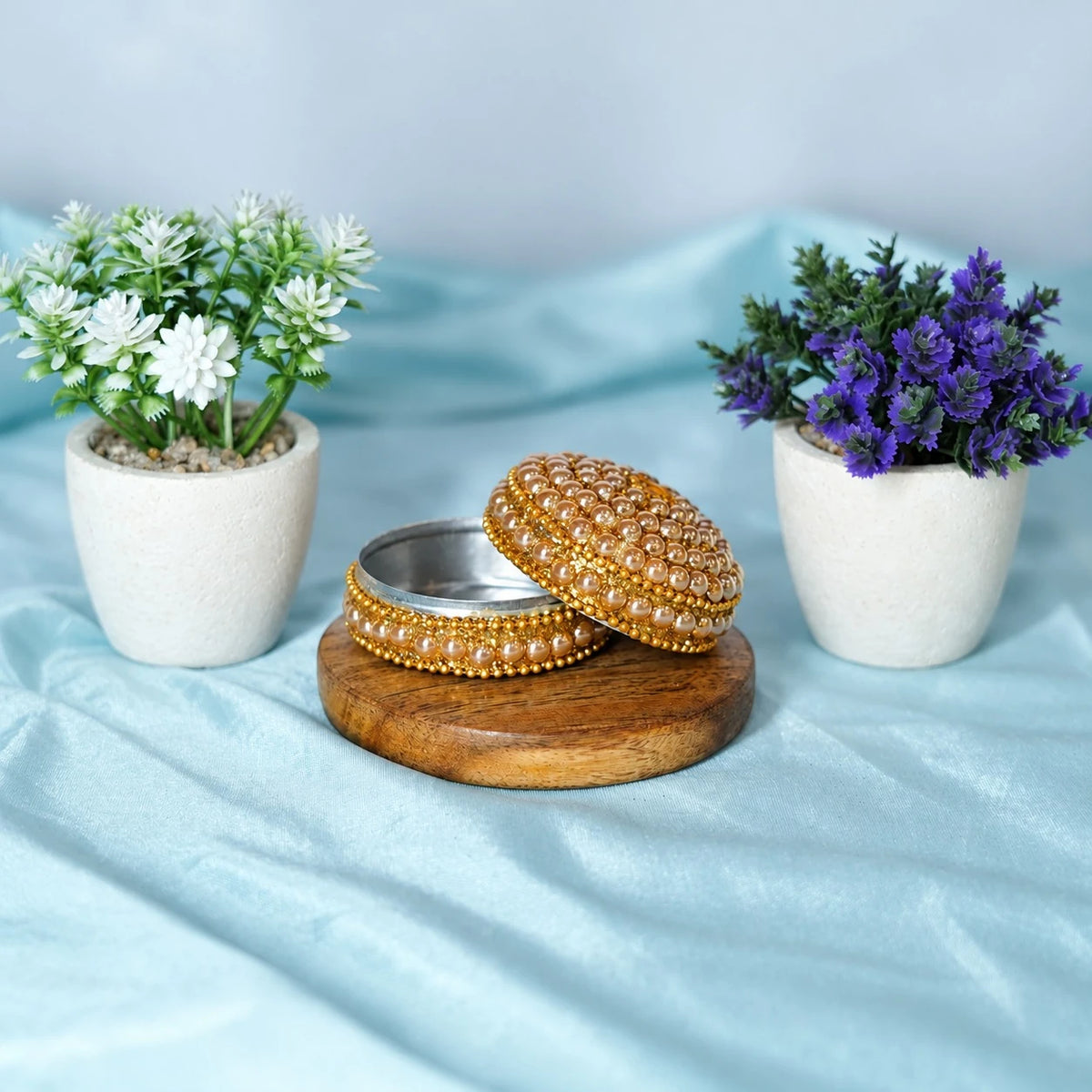Small round beaded pujan dibbi with its lid open beside it, on a wooden base