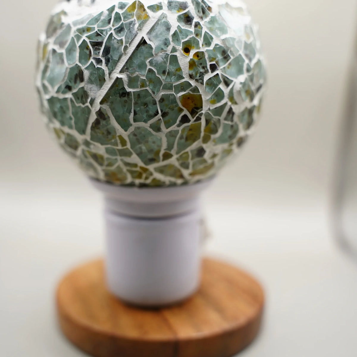 Side view of the electric kapoor dani mosaic glass bowl on a white plug-in base, on a wooden stand