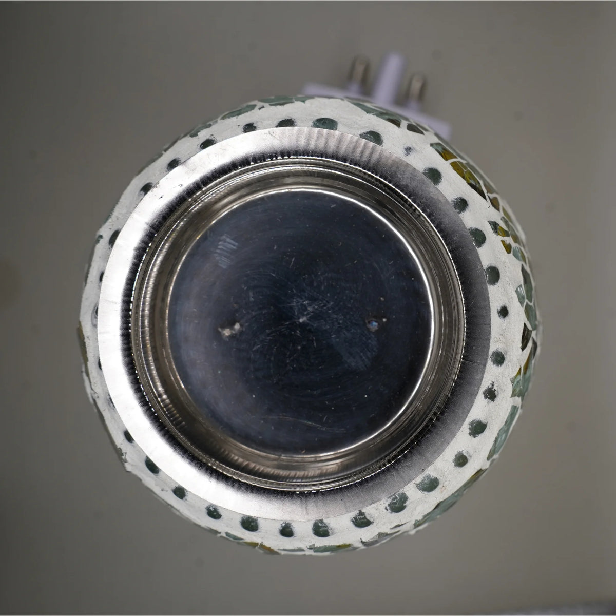 Top view of the steel cup inside the mosaic glass bowl of the electric kapoor dani, with plug pins at the back