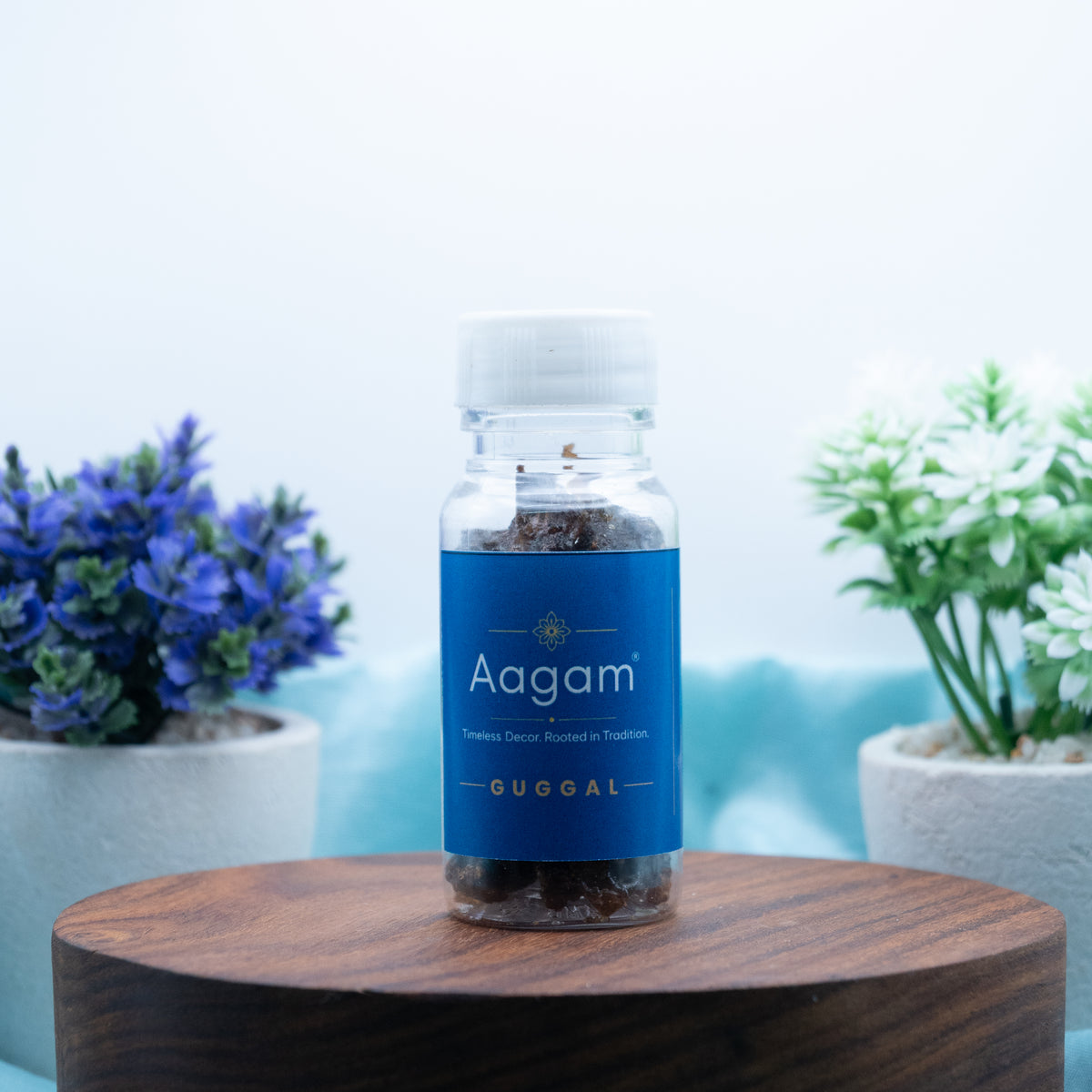 Aagam guggal resin lumps in a clear bottle with a blue label and white cap, shown on a wooden stand